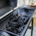 Close-up of a charcoal grill emitting smoke, showcasing burning coals and outdoor cooking setup.