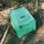 High angle of plastic container with grit on paved surface near entrance of building
