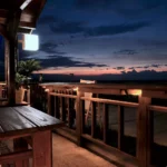 Serene outdoor patio overlooking the ocean at twilight with wooden furniture and gentle ambient lighting.