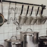 Industrial kitchen setup with hanging utensils and a row of cooking pots.