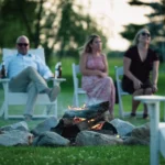 A group of adults enjoying a peaceful evening with a campfire and drinks.