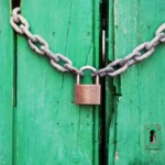 A rustic green wooden door secured with a heavy chain and padlock, symbolizing security.